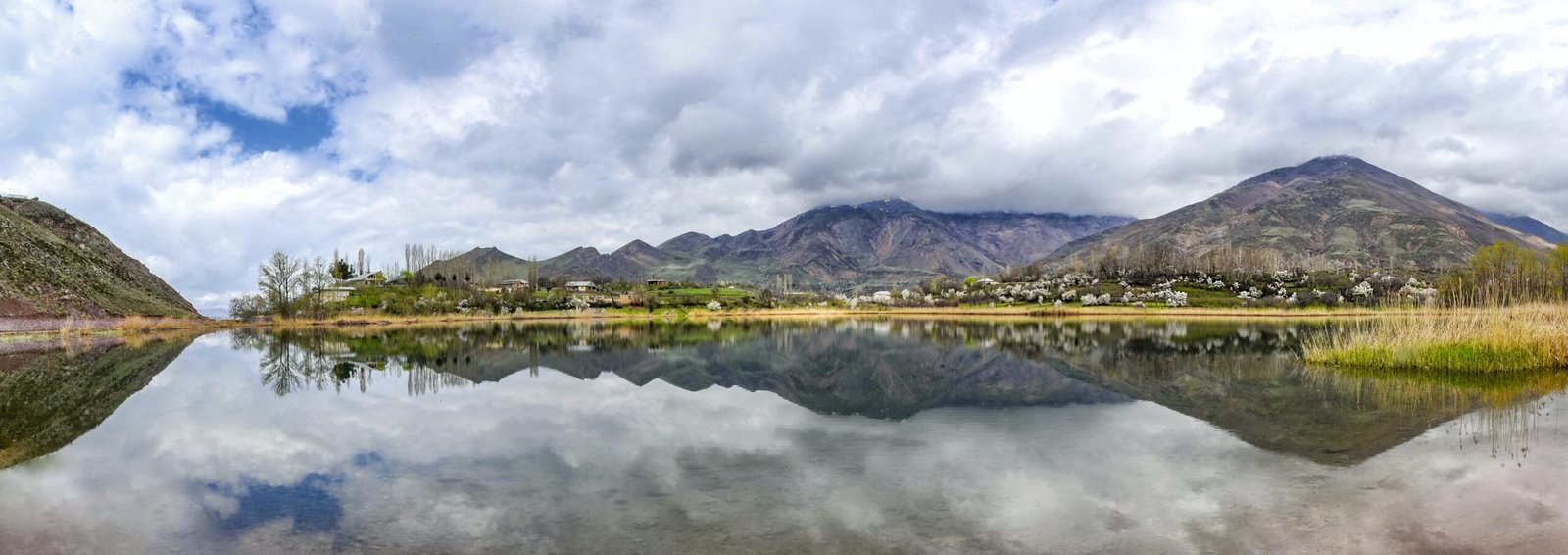 body of water near mountain under cloudy sky during daytime